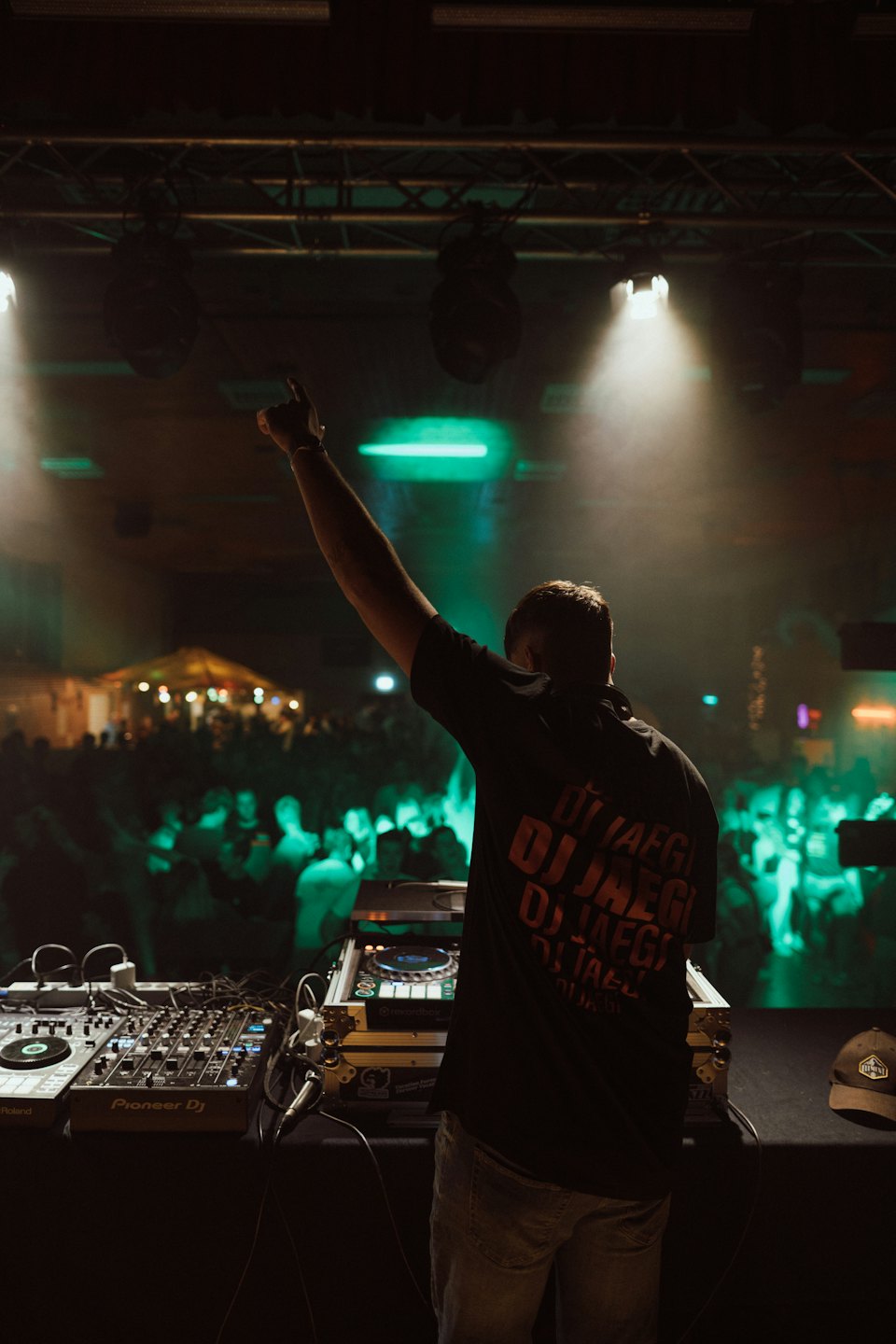 DJ con un braccio alzato sopra l'attrezzatura audio durante un evento notturno.