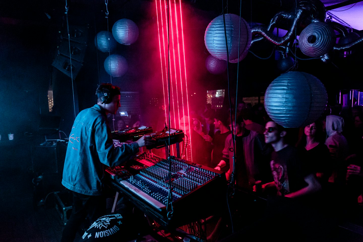 DJ che mixa musica in una discoteca vibrante con luci al neon rosse.